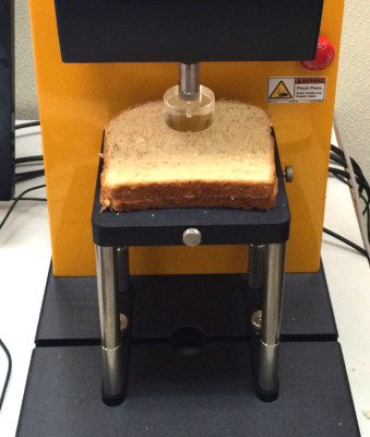 A slice of bread being tested on a texture analyzer.